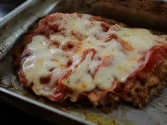 A breaded beef cutlet under melted mozzarella and tomato, the browned crumb edge still visible around the rim.