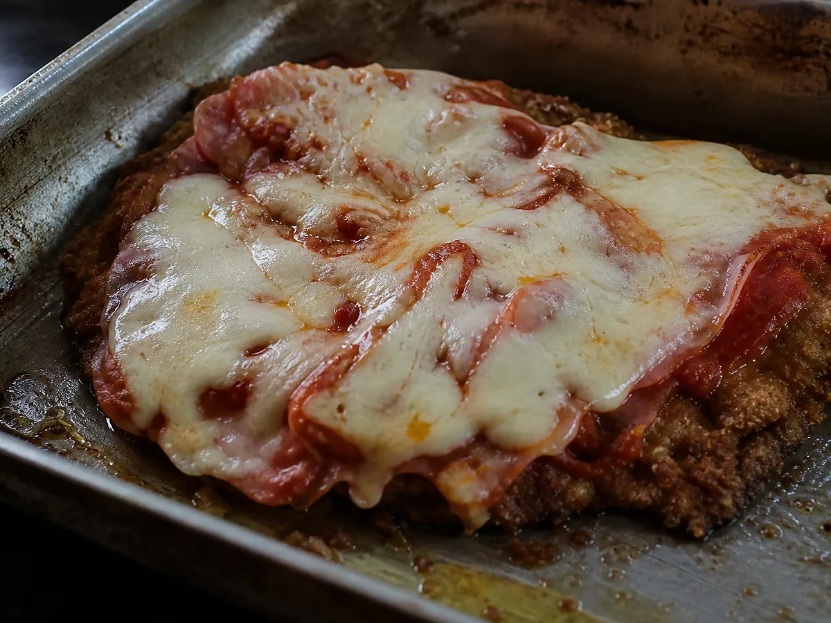 A breaded beef cutlet under melted mozzarella and tomato, the browned crumb edge still visible around the rim.
