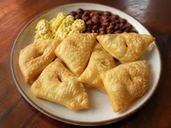 Six puffed golden fry jacks on a plate with scrambled eggs and a spoonful of stewed black beans.