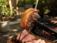 A grilled picanha with a browned, blistered fat cap, part-sliced against the grain to show a pink centre.