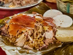 Sheets of amber crackling laid over shredded roast pork and yellow rice studded with peas, served on a banana leaf, with pale rounds of arepa and a wedge of soft white cheese to one side.