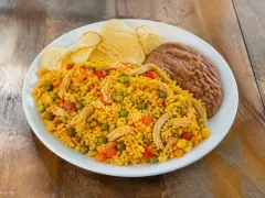 A white plate of golden-yellow rice studded with shredded chicken, green peas, sweet corn, red pepper and diced carrot, with ruffled potato crisps and a disc of refried black beans alongside.