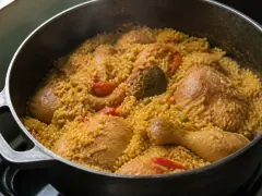 A pot of yellow Cuban arroz con pollo with browned bone-in chicken pieces, green peas, and strips of roasted red pepper on top.