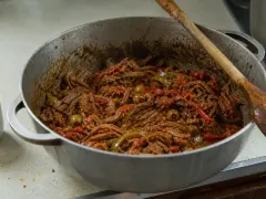 Long shreds of beef in a rust-red pepper and tomato sauce, scattered with green olives, over white rice.