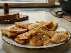 Golden twice-fried plantain discs on a rack, edges blistered and cracked, scattered with coarse salt.