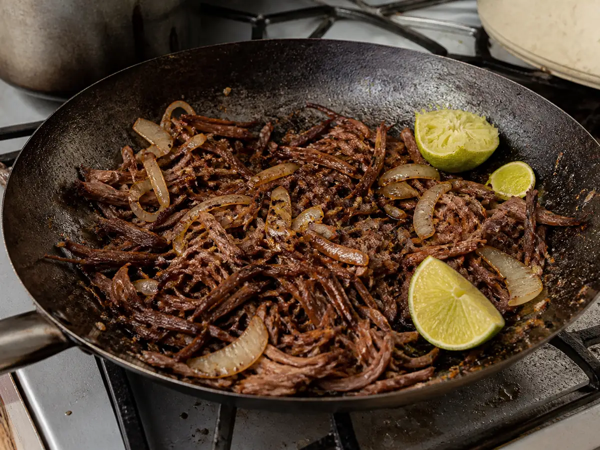 Crisp-edged shreds of fried beef with wilted onion half-moons and a lime wedge, the crust visibly mahogany in places.