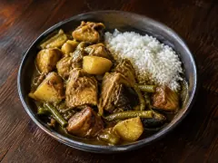 Golden colombo stew with browned pork, potatoes, eggplant, green beans and mango beside a mound of white rice.