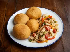 Four puffed golden fried bakes beside a pile of flaked saltfish sautéed with tomato, onion and red and orange peppers.