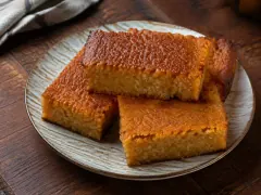 Three squares of cassava pone with crisp orange-brown tops and a dense golden coconut crumb, stacked on a plate.