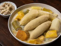 Metemgee of pale duff dumplings, cassava, plantain and pumpkin in a creamy coconut broth, with a small dish of shredded saltfish behind.