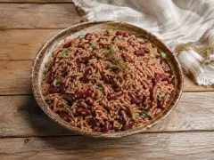 A rustic bowl of rosy-brown rice studded with whole dark red kidney beans and flecks of green scallion, topped with a sprig of thyme, on a wooden table.
