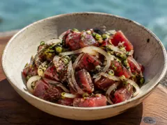 A bowl of ruby-red cubes of raw tuna tossed with slivers of sweet onion, green scallion and dark flecks of seaweed and sesame, by the sea.
