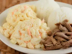 Two scoops of creamy macaroni salad flecked with orange carrot beside white rice and shredded kalua pork on a plate-lunch plate.