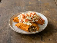 Two orange fried corn turnovers on a speckled plate, one split to show a ground-beef and rice filling, the other buried under shredded cabbage and red sauce.