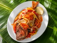 A whole fried red snapper with blistered golden skin, heaped with pickled julienned carrot, onion rings, red pepper strips and Scotch bonnet ribbons.