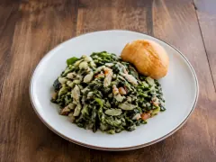 A skillet of glossy dark green callaloo ribbons tossed with white flakes of salt cod, diced tomato and scallion, with no liquid pooled in the pan.