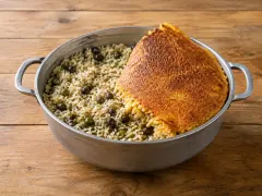 An aluminium pot of pale coconut rice studded with dark green pigeon peas, with a large sheet of deep golden-brown crisp crust lifted and propped across one side.