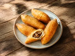 Four golden deep-fried torpedo-shaped croquettes with tapered ends on a speckled grey plate, one split open to show a dark spiced ground-beef filling.