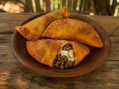 Three deep golden-orange fried turnovers with crimped edges on a round terracotta plate, the front one broken open to show minced beef and a piece of hard-boiled egg white, on a weathered wooden table.