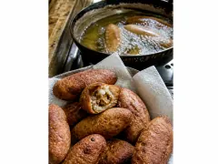 Fried alcapurrias on a rack, deep gold and blistered, one broken open to show the orange masa wall and beef filling.