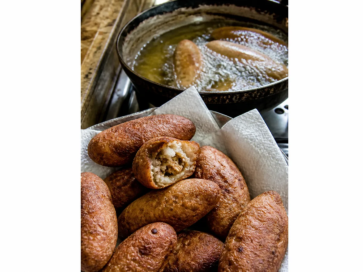 Fried alcapurrias on a rack, deep gold and blistered, one broken open to show the orange masa wall and beef filling.