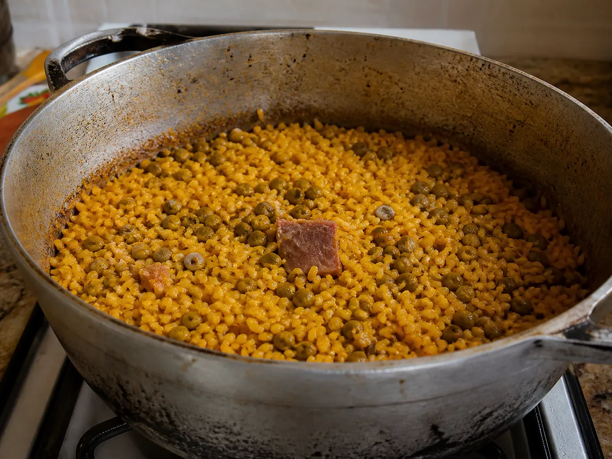 A pot of orange-stained rice studded with whole pigeon peas, diced ham, and green olives.