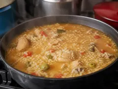 A bowl of asopao de pollo — soupy orange rice with a bone-in chicken thigh, green olives, and cilantro.