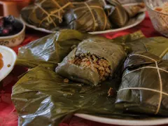 Pasteles unwrapped from their banana leaves, the orange masa set around a dark pork filling, with tied packets stacked behind.
