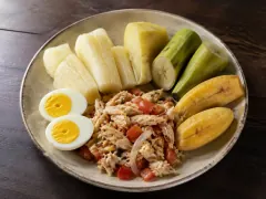 A her'heri plate of boiled cassava, sweet potato, green and ripe plantain, halved boiled eggs and flaked salt cod with tomato and onion.