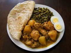 A Surinamese roti plate: a folded rotiplaat, chicken and potato in yellow massala gravy, sautéed kouseband beans and a halved boiled egg.