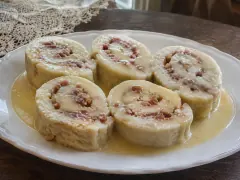 Five pale slices of rolled guava duff, each with a pink spiral of guava, in a pool of butter and rum sauce on a white oval platter.