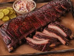 A rack of smoked baby back ribs with a sticky, glossy mahogany glaze and bones pulling back from the meat, sliced into individual ribs on a board.