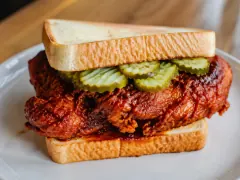 Pieces of fried chicken glazed a deep crimson red with a crackly crust, resting on slices of soft white bread with crinkle-cut pickles on toothpicks.