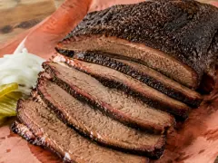 Thick slices of smoked brisket with a black pepper bark and a bright pink smoke ring fanned on butcher paper, glistening with rendered fat.