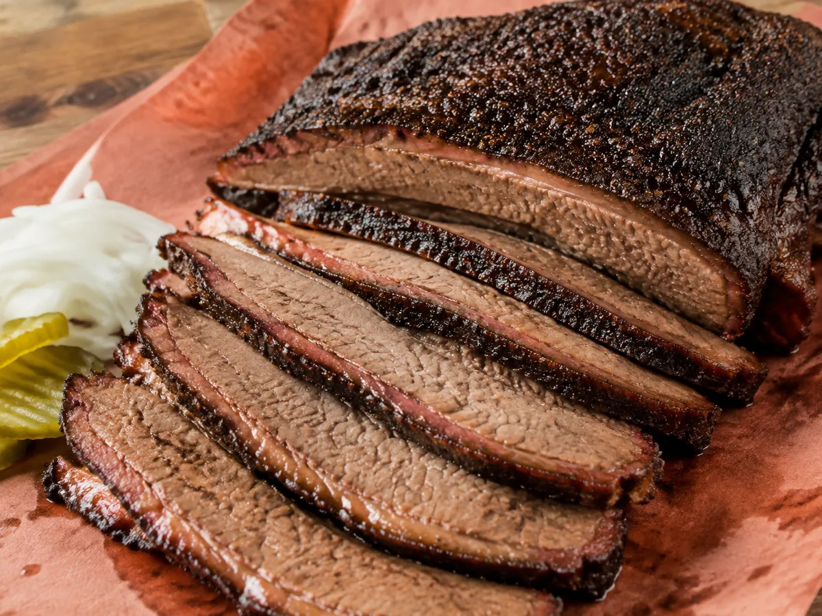 Thick slices of smoked brisket with a black pepper bark and a bright pink smoke ring fanned on butcher paper, glistening with rendered fat.