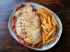 A large breaded beef cutlet under a blistered layer of melted mozzarella, ham and tomato sauce dusted with oregano, with a pile of golden chips beside it.
