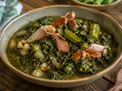 A bowl of thick dark-green kallaloo with pieces of crab, pink ham, okra and pale conch in the greens.